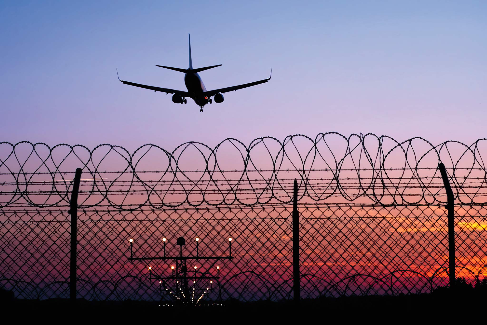 Airplane landing at night behind fence.