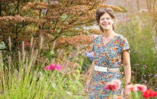 Exterior photo of a smiling Carina Weijma standing among flowers in a luscious park.