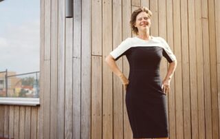 Exterior photo of a smiling Carina Weijma standing in front of a modern wooden building.