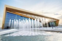 Modern venue with huge glass walls, with a fountain in the foreground.