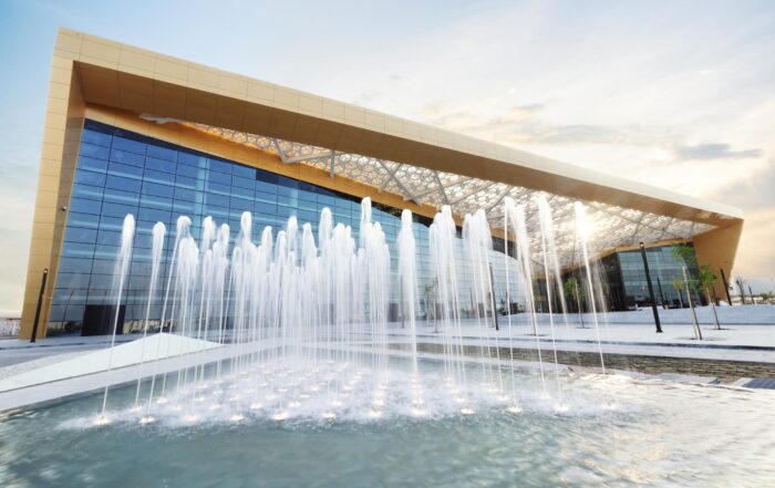 Modern venue with huge glass walls, with a fountain in the foreground.